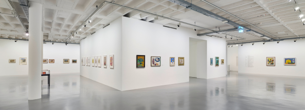 Ausstellungsraum mit gerahmten Gemälden an weißen Wänden und spiegelndem Boden.