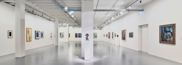 Ausstellungsraum mit Gemälden an weißen Wänden und einer Skulptur auf Sockel im Zentrum.
