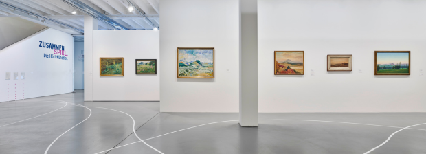 7.	Blick durch den Ausstellungsraum mit Landschaftsbildern und geschwungenen weißen Linien am Boden. 