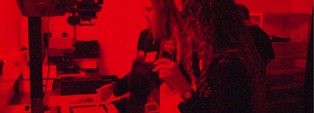 Kinder arbeiten im rot beleuchteten Fotolabor an fotografischen Experimenten.