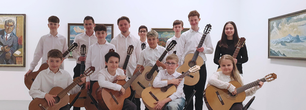 Jugendliches Gitarrenensemble posiert mit Instrumenten vor Gemälden im Ausstellungsraum.