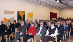 Menschen sitzen im bestuhlten Ausstellungsraum bei Ausstellungseröffnung