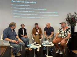 Frontalansicht von Personen auf Stühlen diskutieren bei Podiumsdikussion 