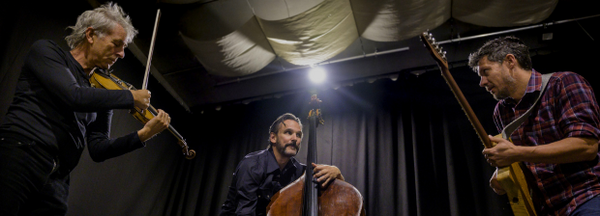 Drei Musiker mit Violine, Kontrabass und Gitarre improvisieren auf Bühne, Spotlicht.