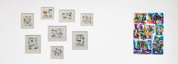 Mehrere kleine abstrakte Zeichnungen und ein großes farbiges Bild an weißer Wand.