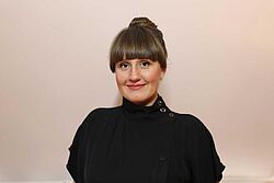 Frau vor weisser Wand blickt lächelnd den Betrachter an