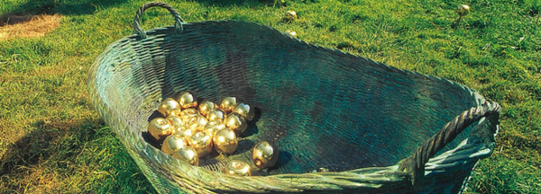 Korb aus Metall mit goldenen Äfpfeln im Park 